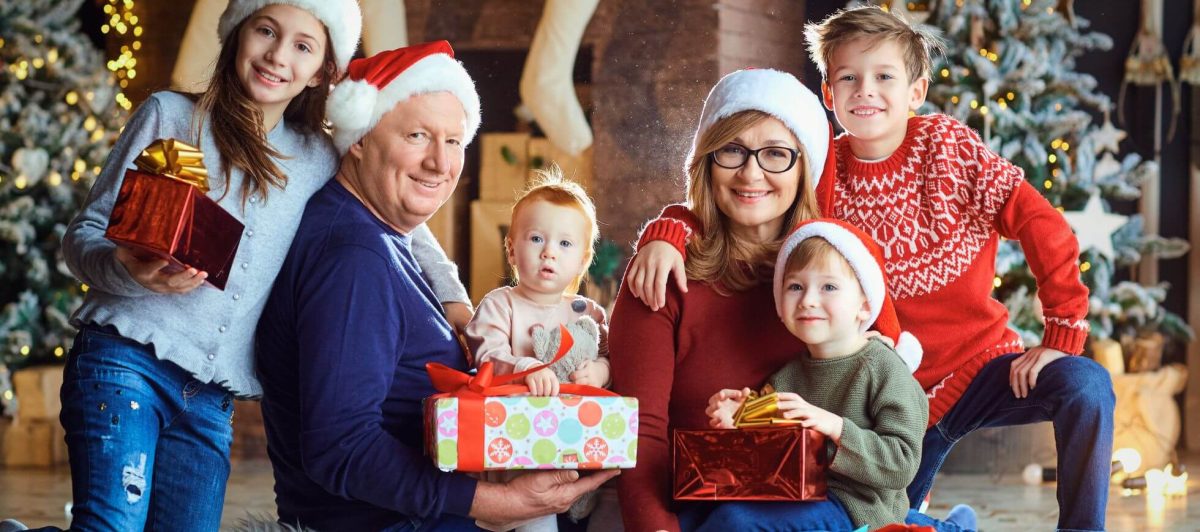 A happy white family sat in Christmas jumpers and hats gifting to each other.