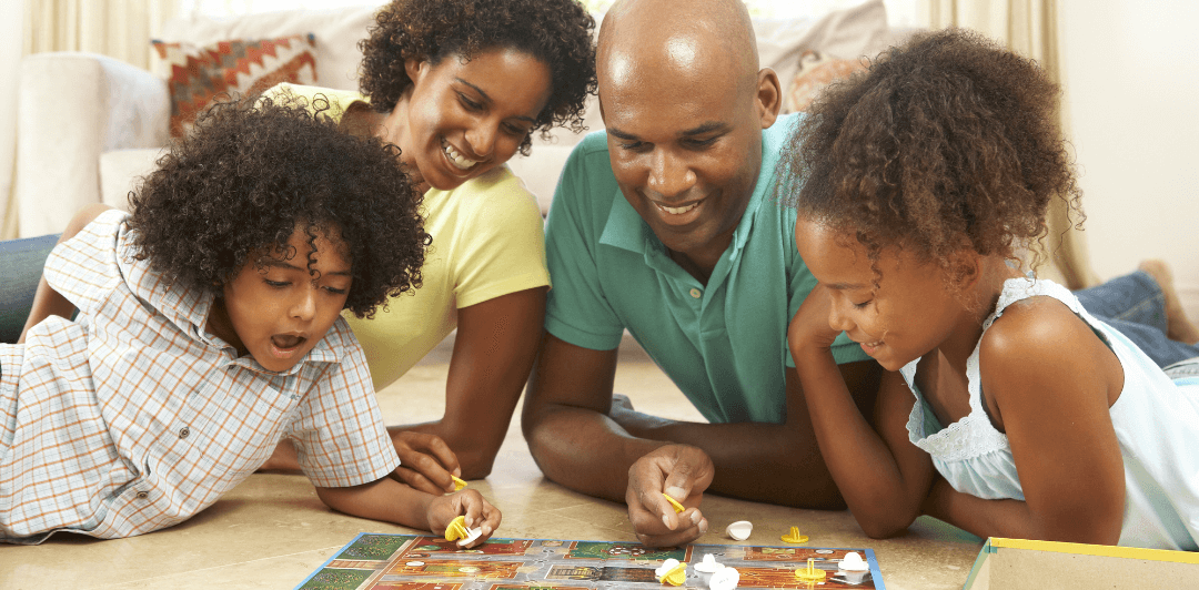 A family of four, two adults and two children, playing money-themed board games